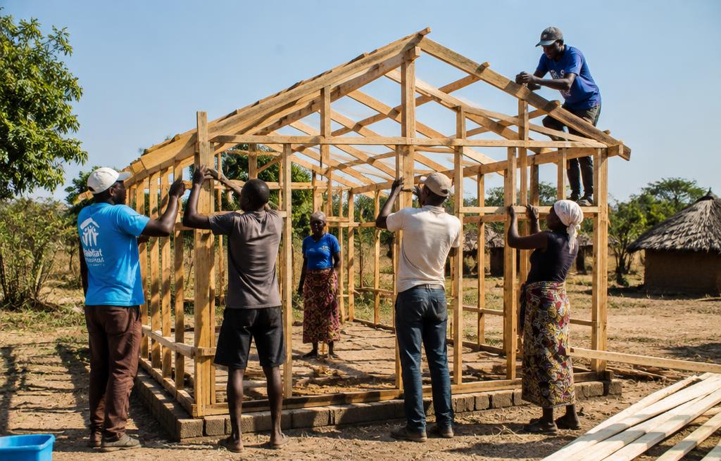 Volunteers raising the wooden frame of a home in rural Zambia